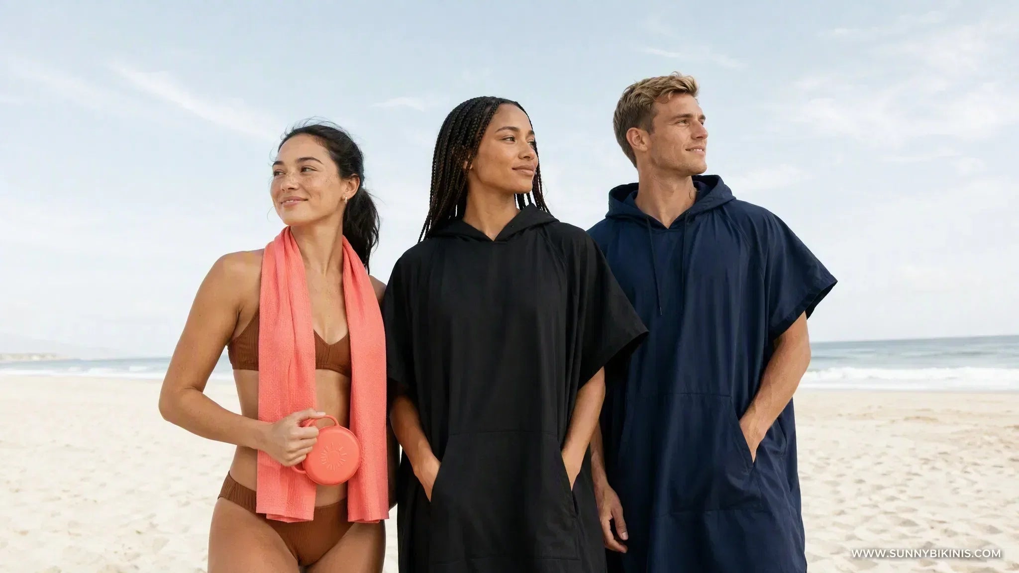 Three functional beach towels laid on light sand: cooling towel, hooded poncho, and surf changing robe
