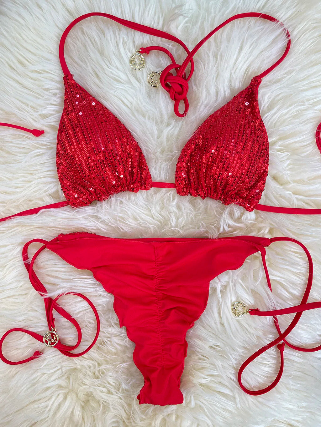 Red sequin triangle bikini top and solid satin ruffle thong bottom on white fur rug
