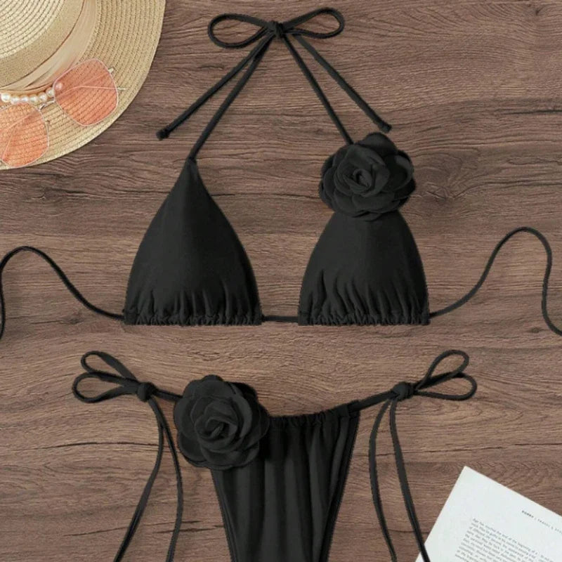 Black halter string bikini with 3D rose and bow tie straps laid flat with a sun hat
