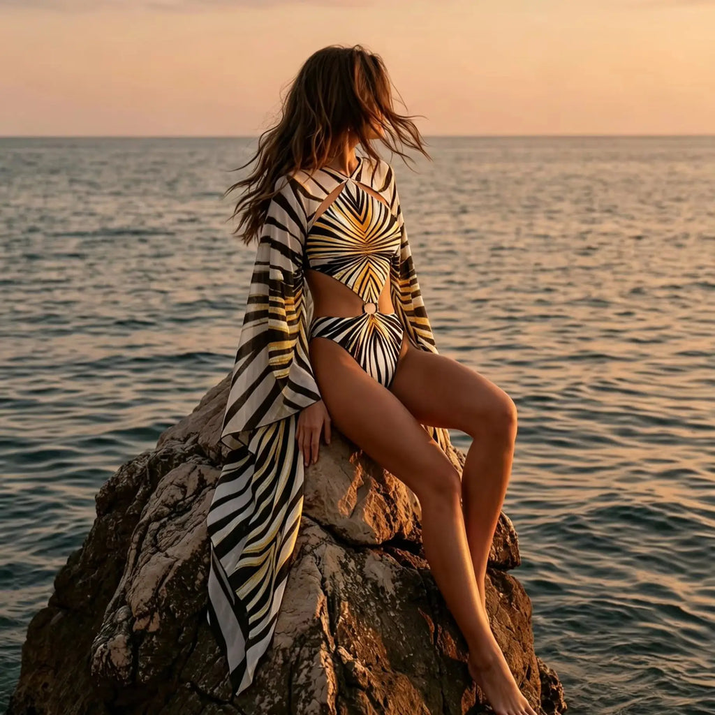 Model in a black and gold print one piece swimsuit with sheer cover up at the beach