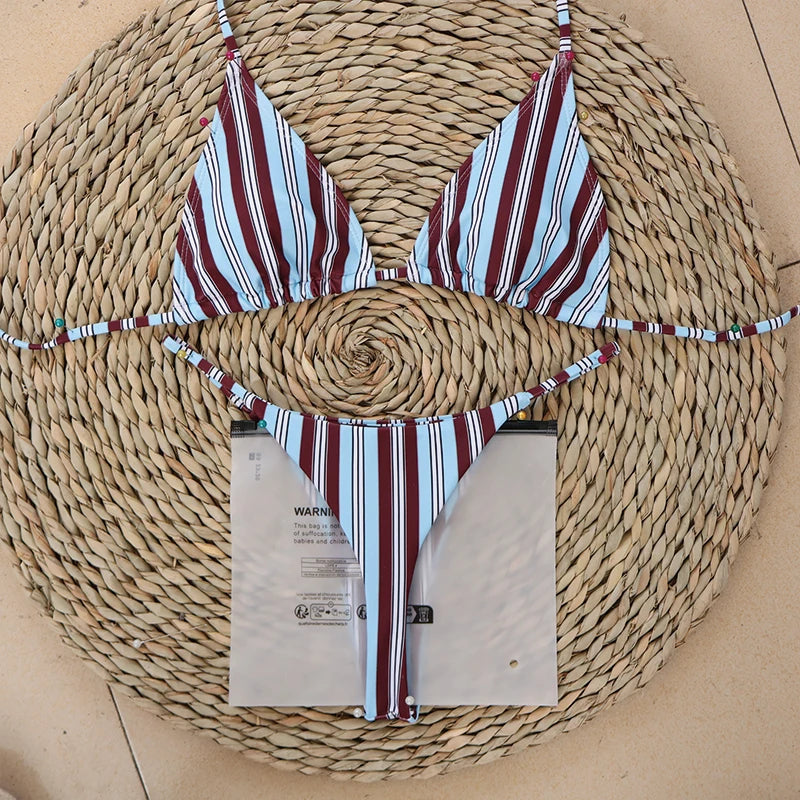 Burgundy, white and blue striped bikini top and tie-side bottoms laid flat on a straw mat