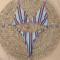 Burgundy, white and blue stripe bikini set with tie sides laid flat on a straw mat