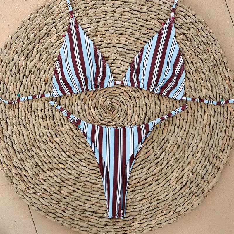 Burgundy, white and blue stripe bikini set with tie sides laid flat on a straw mat