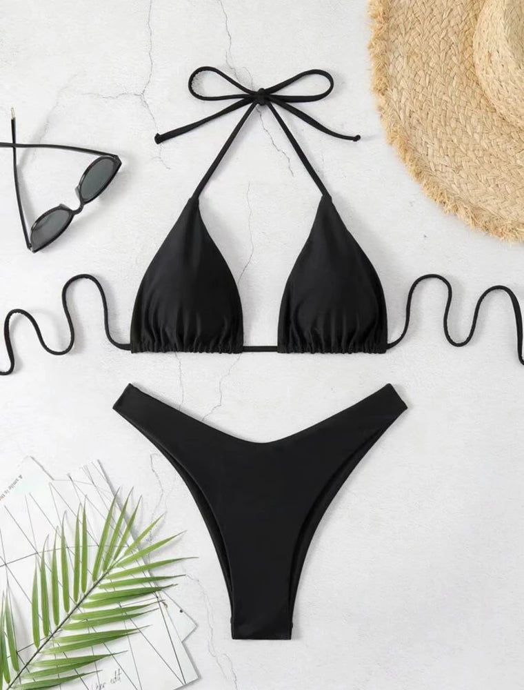 Black ruffle halter bikini set with tie neck straps and high cut thong bottom on white marble