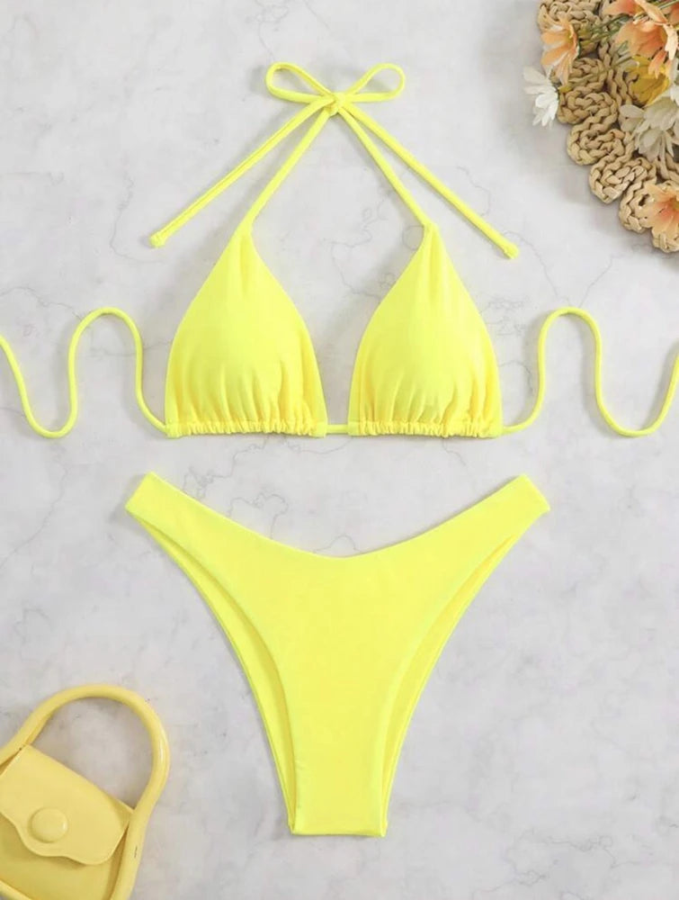 Yellow ruffle halter bikini set with neck tie bow and high cut thong bottom on white marble