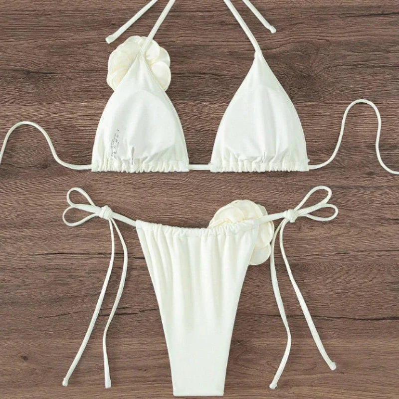 White halter bikini top and tie side bottom with 3D rose shown from the side on wood