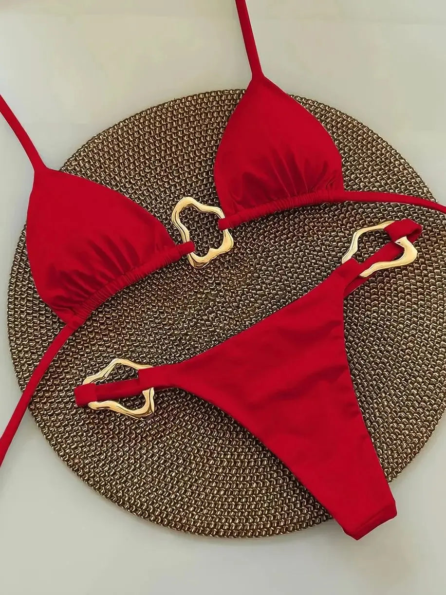Red halter micro bikini set with metal ring detail, flat lay on woven mat