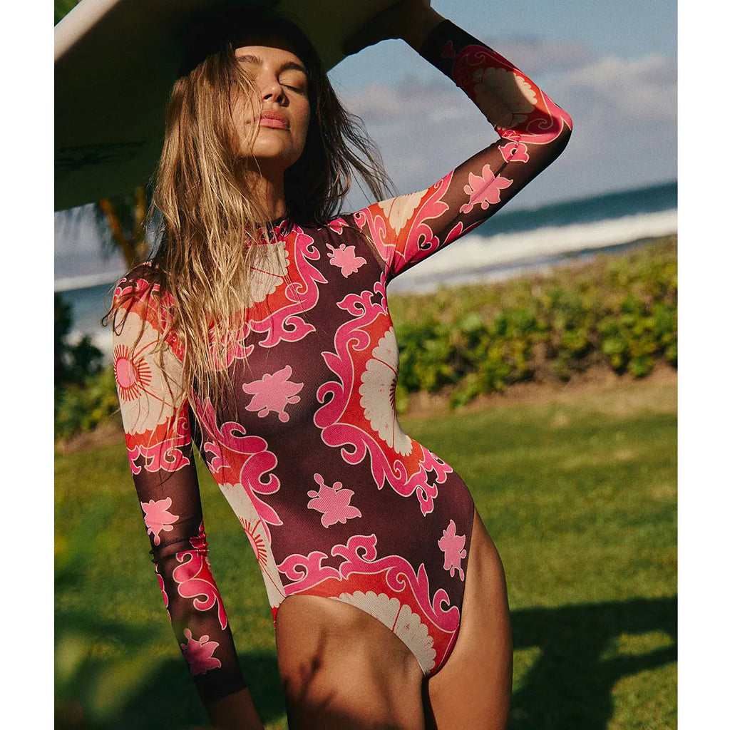 Woman in wine floral long sleeve monokini on the grass with a surfboard