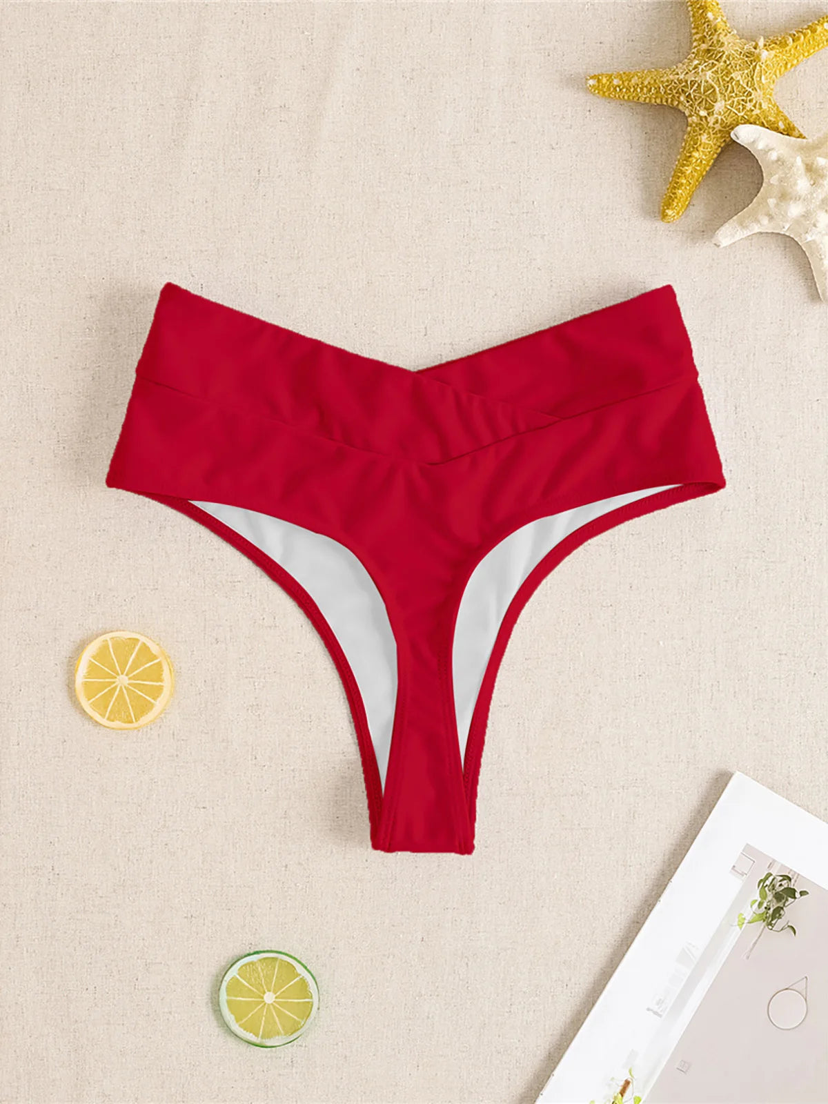Red high waist crossed waistband Brazilian bikini bottom flat on beige linen with starfish props