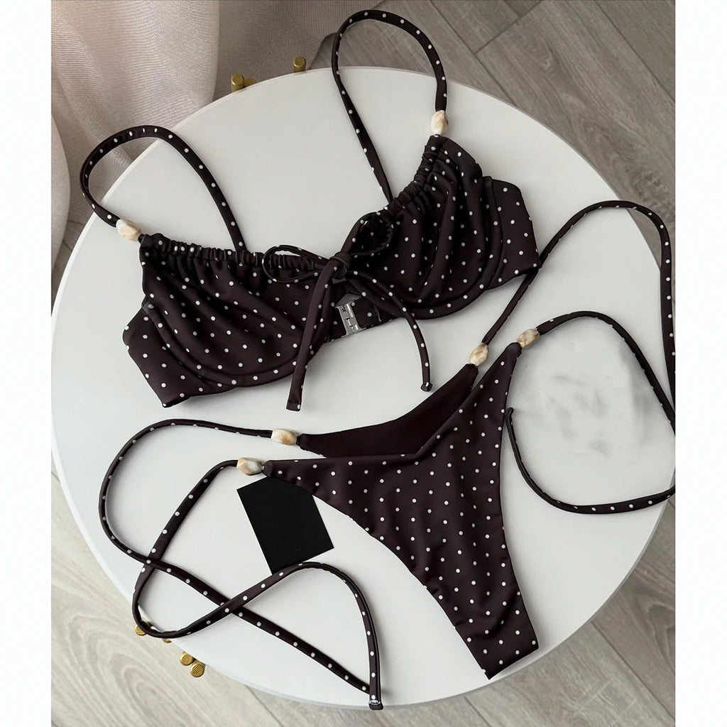 Brown polka dot string bikini with ruffle top, beaded straps, and tie thong bottom laid on a white marble table