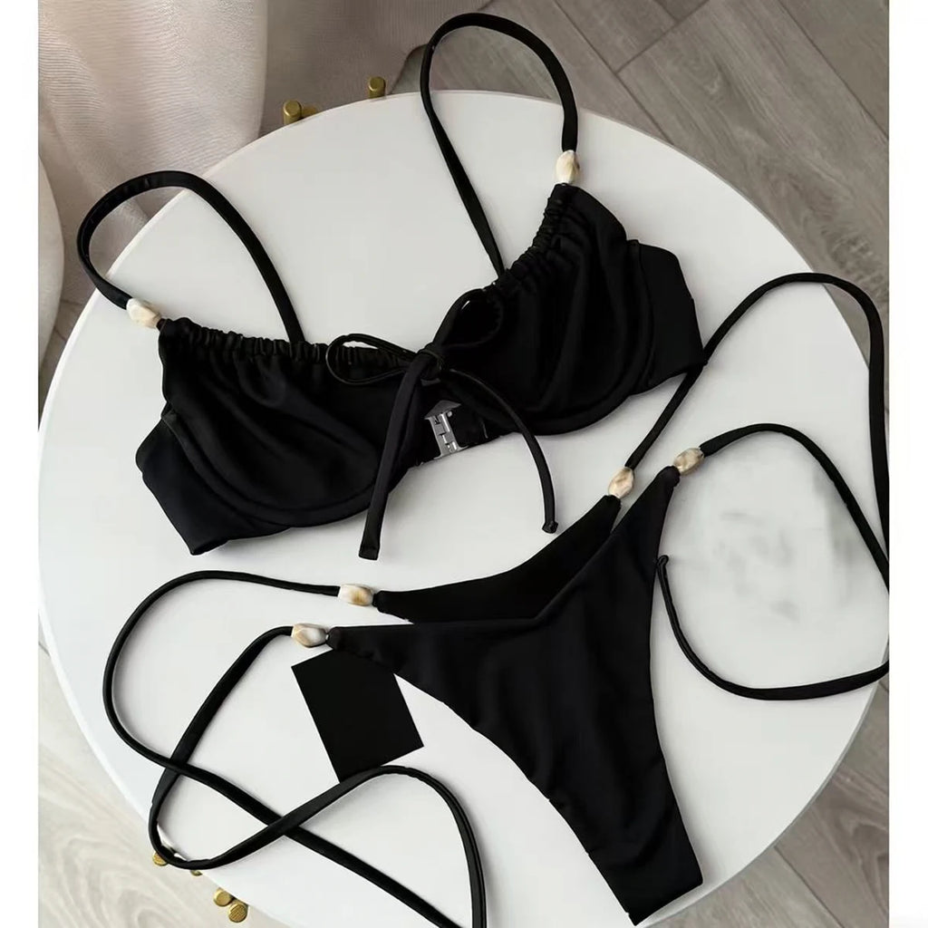 Black string bikini with gathered ruffle cups, beaded neck ties, and thong bottom on white marble