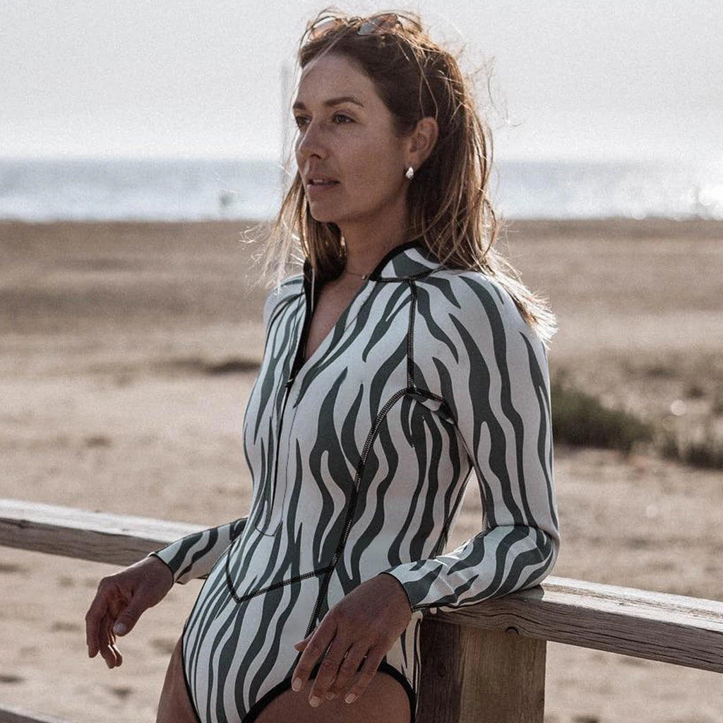 Woman in grey zebra long sleeve monokini leaning on a beach fence