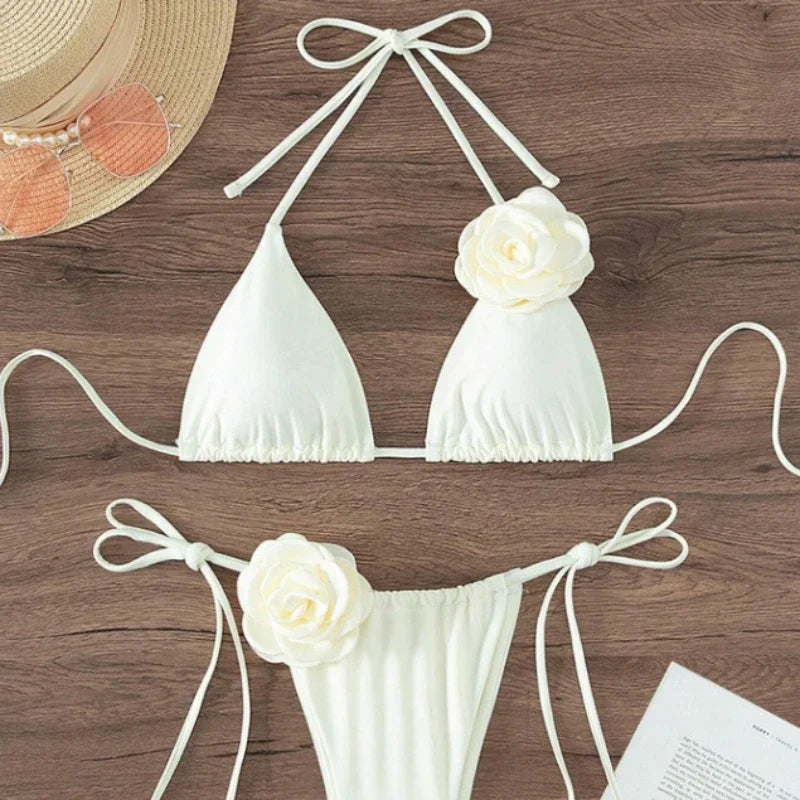 White halter string bikini with 3D rose and bow tie straps laid flat with a sun hat
