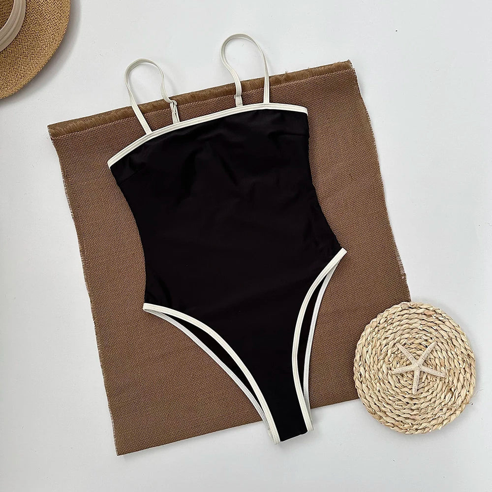 Black retro one piece swimsuit with contrast trim laid on burlap next to a woven fan