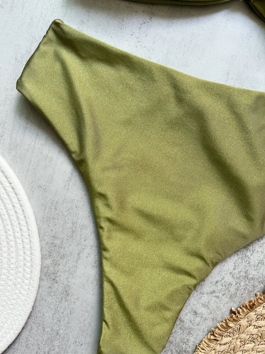 Olive green Brazilian cut bikini bottom flat lay on marble surface