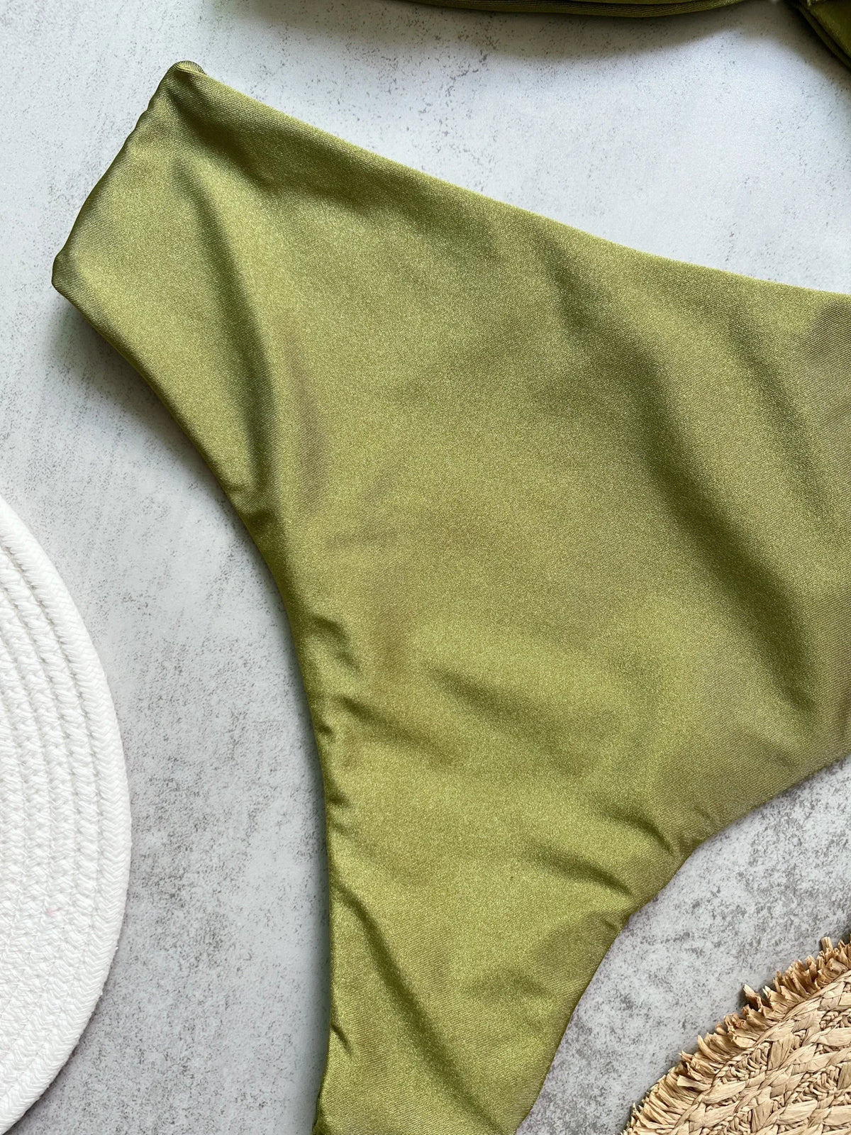 Olive green Brazilian cut bikini bottom flat lay on marble surface