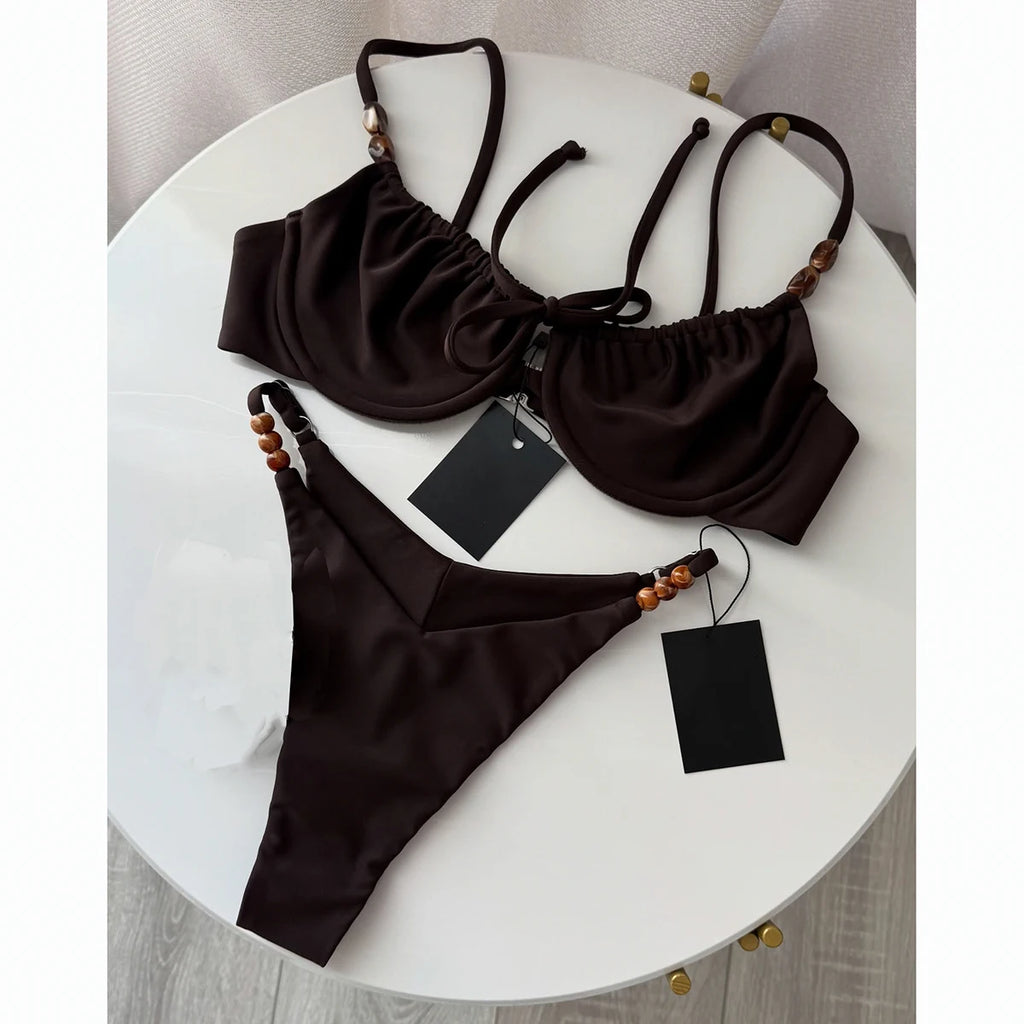 Solid dark chocolate string bikini with ruffle top and shell beaded ties on a white marble table