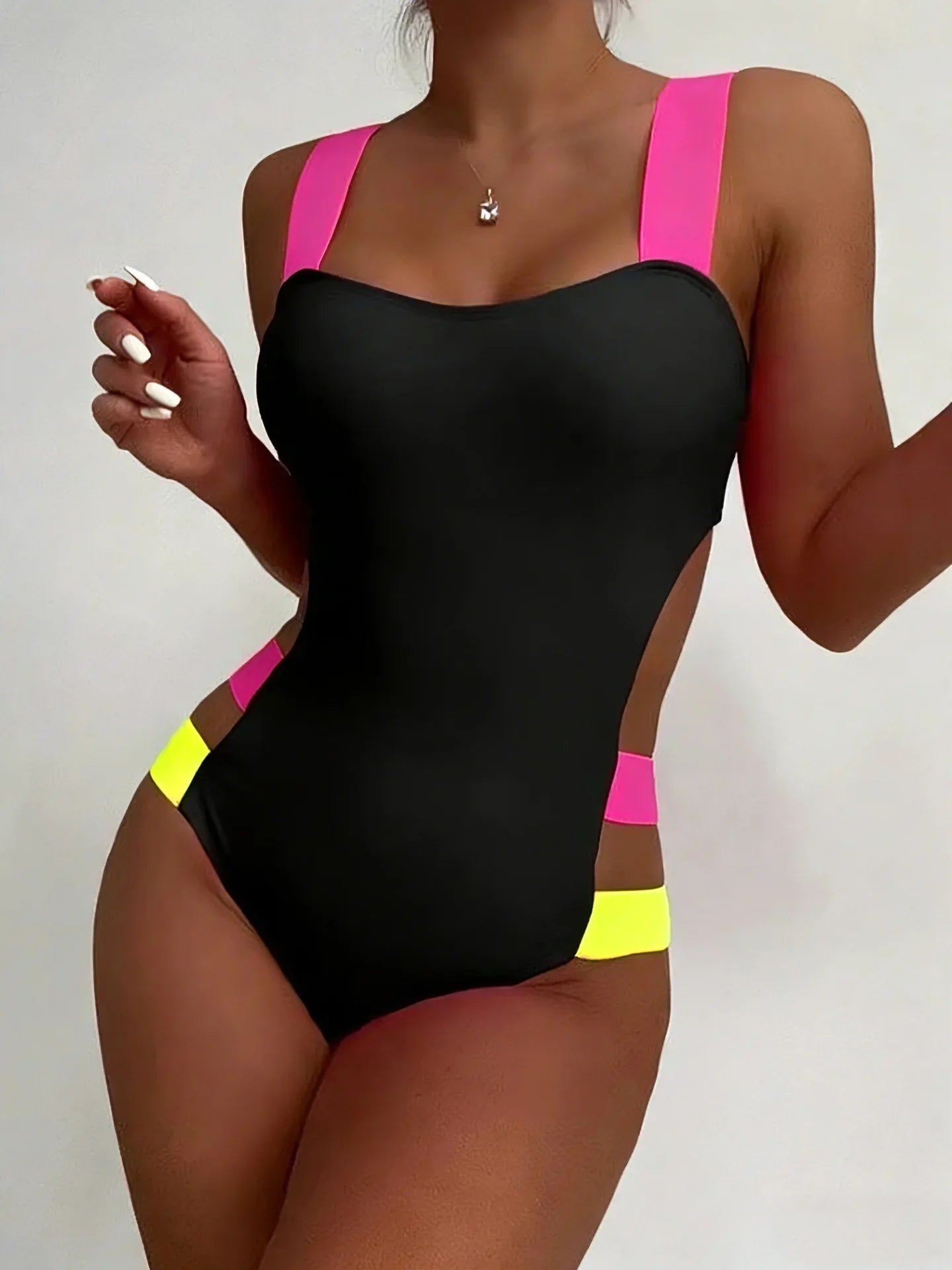 Black one-piece swimsuit with neon pink and yellow straps and a hollow back design shown from the back side