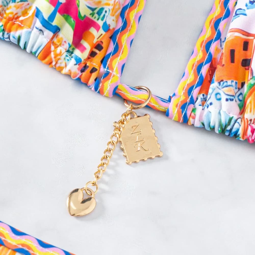 Gold-toned charm with rectangular zk tag and heart pendant on colorful fabric of floral push‑up triangle bikini set with brazilian bottoms