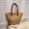 Khaki woven straw beach tote with brown leather handles and two front straps