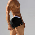 Black low-waist swim trunks with white waistband and round side logo